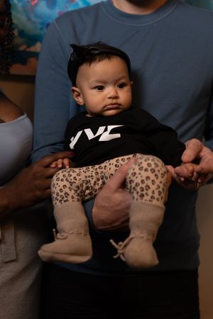 Baby wearing leopard print booties being held in someone's lap.