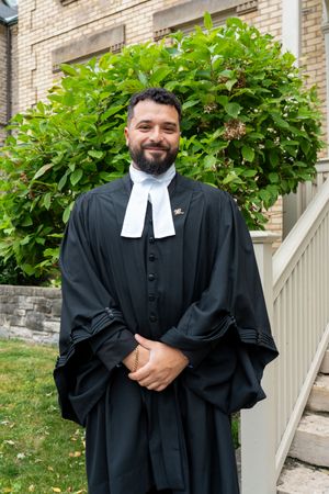 People wearing traditional black academic graduation robes posed in front of brick building and greenery.