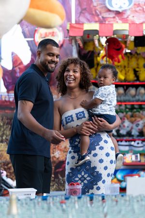 Family enjoying time together at a carnival with colorful game booths in the background.