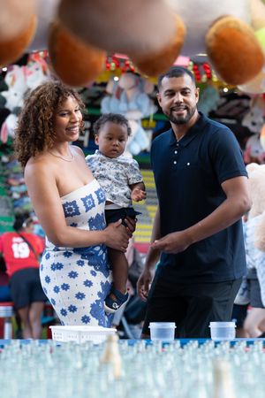 Family moment captured at a carnival with game booths and prizes visible behind them.