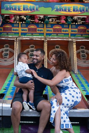 Family sitting at a Skee Ball arcade game booth at a carnival or fair.