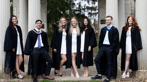 Group portrait of graduates in academic regalia posing between white columns.