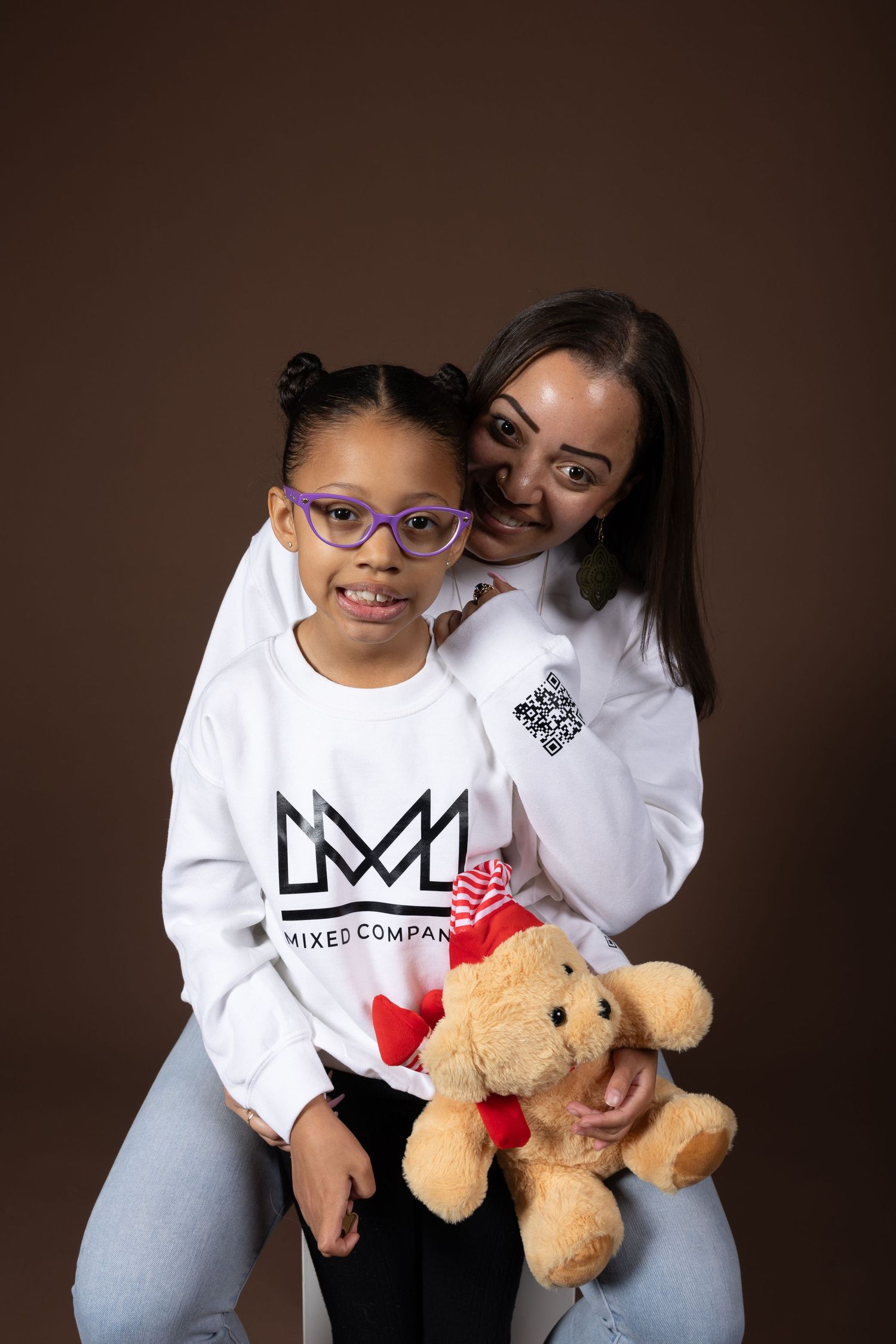 Family portrait showing matching outfits and a teddy bear against brown backdrop.
