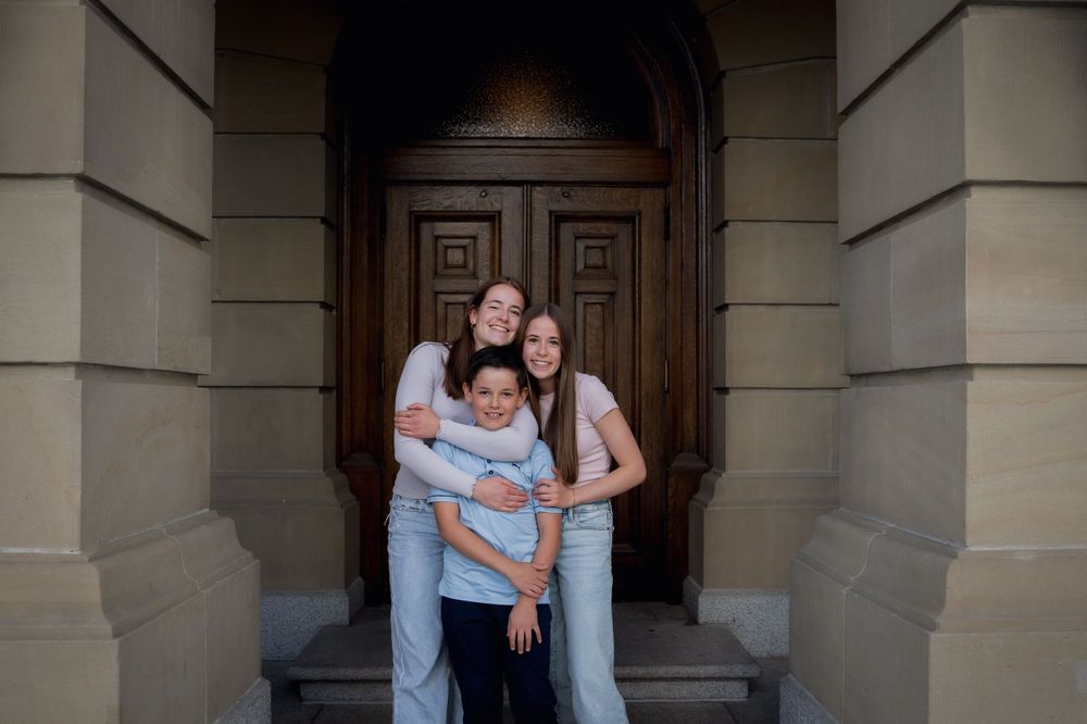 Family shares intimate moment together in archway of historic stone building.