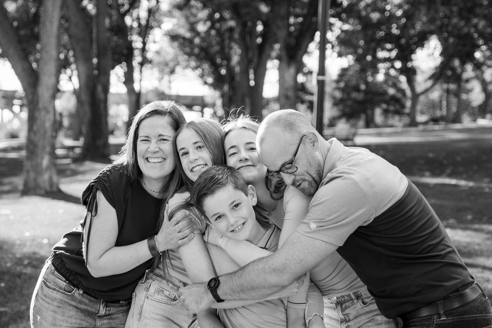 Black and white photo of group sharing joyful embrace outdoors among trees.