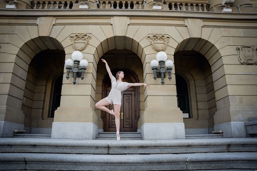 Ballet dancer in white leotard strikes elegant pose on historic building steps.