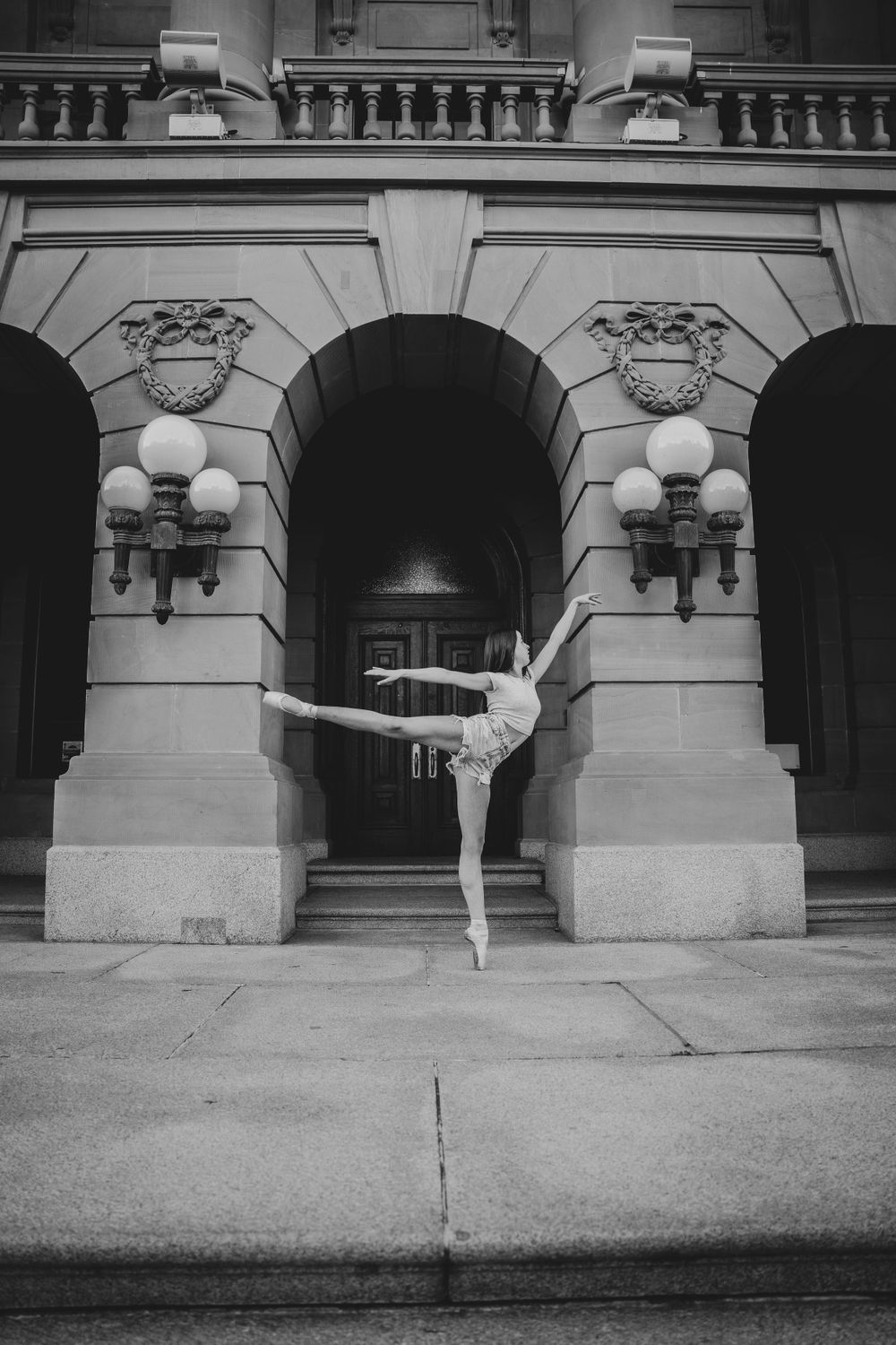 Ballet dancer executes arabesque pose against classical architectural backdrop.