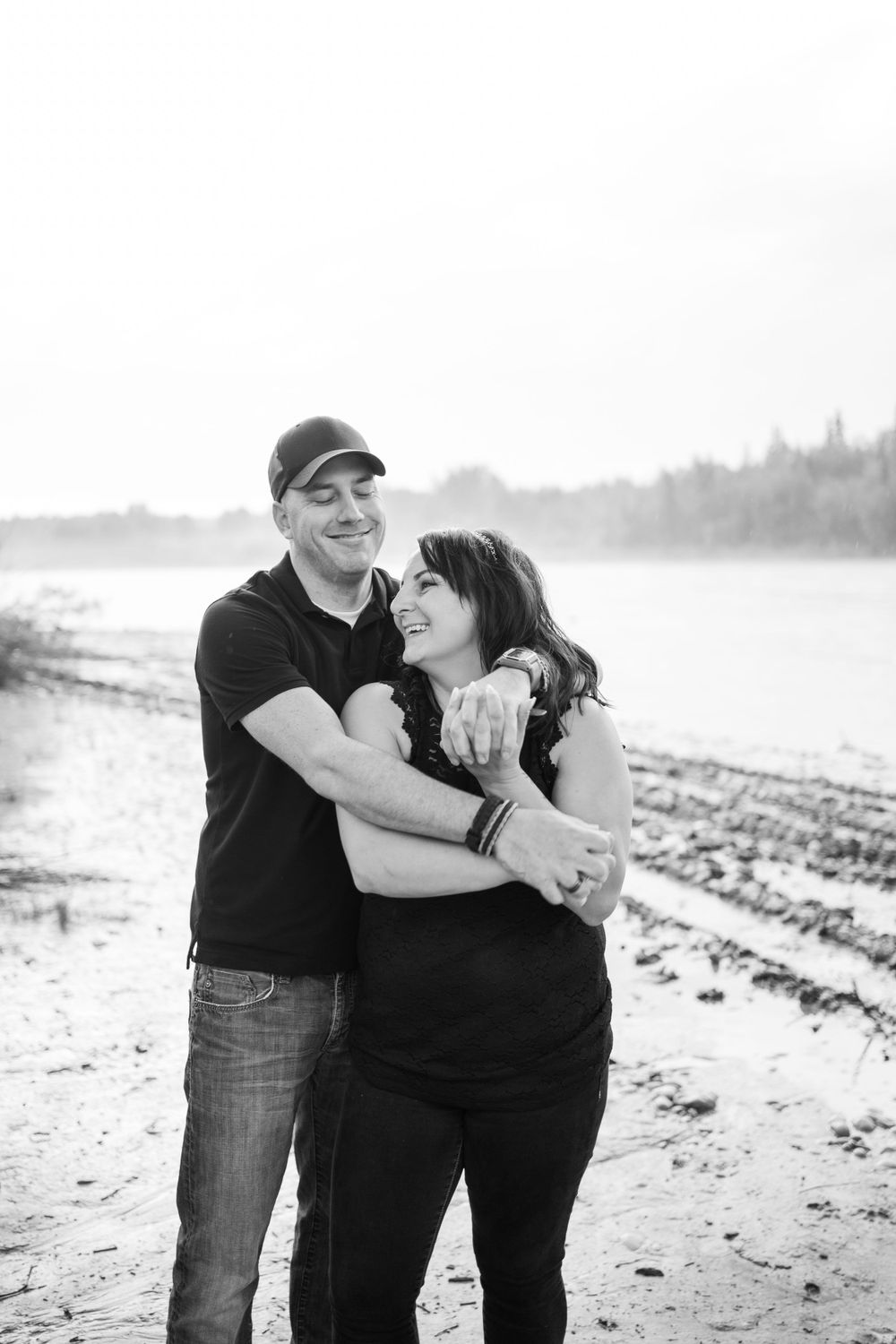 Couple embraces while sharing tender moment on beach shoreline in black and white.