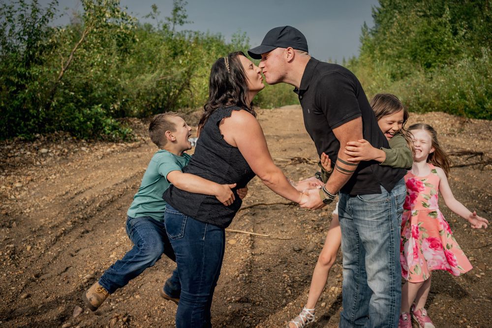 Family plays and shares a loving moment together on a dirt path surrounded by greenery.