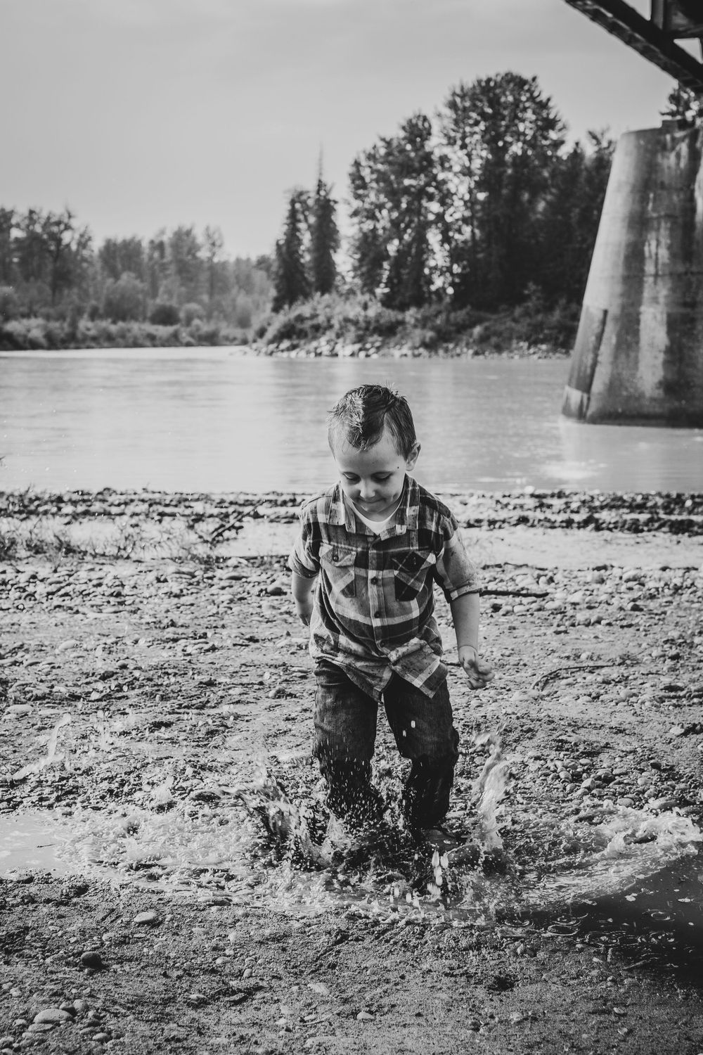 Child splashing and playing in shallow water near bridge support structure.