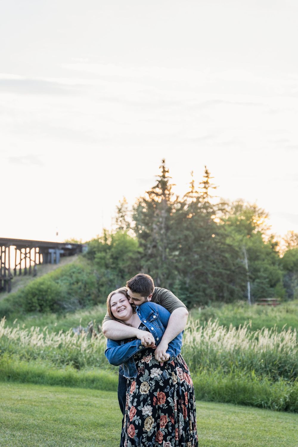 Couple embraces in tender moment on grassy field during golden hour.