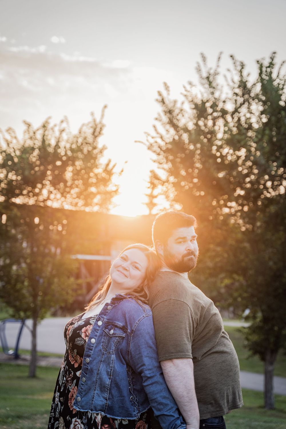 Couple poses back-to-back against sunset in park setting.