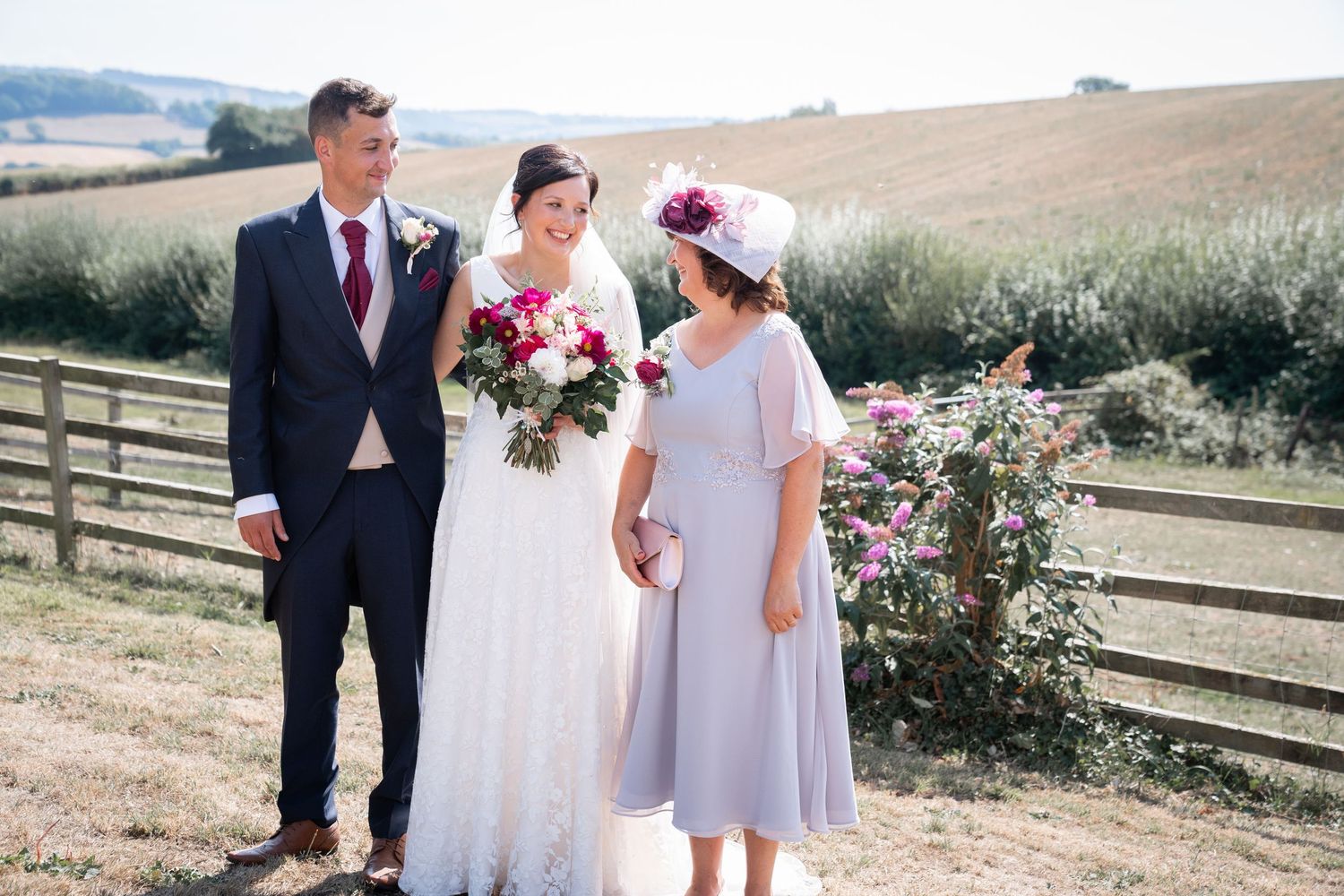 A wedding couple and their wedding party walk along a rustic countryside path on a sunny summer day.