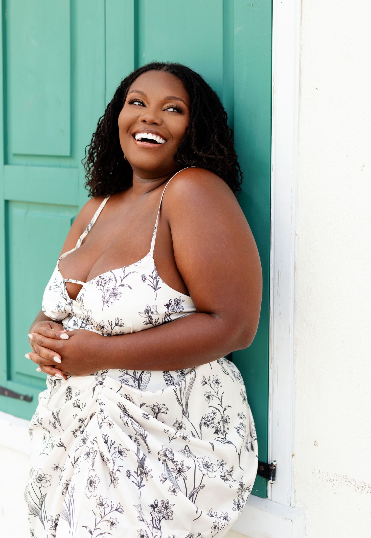 Woman in floral dress laughs joyfully against turquoise door.