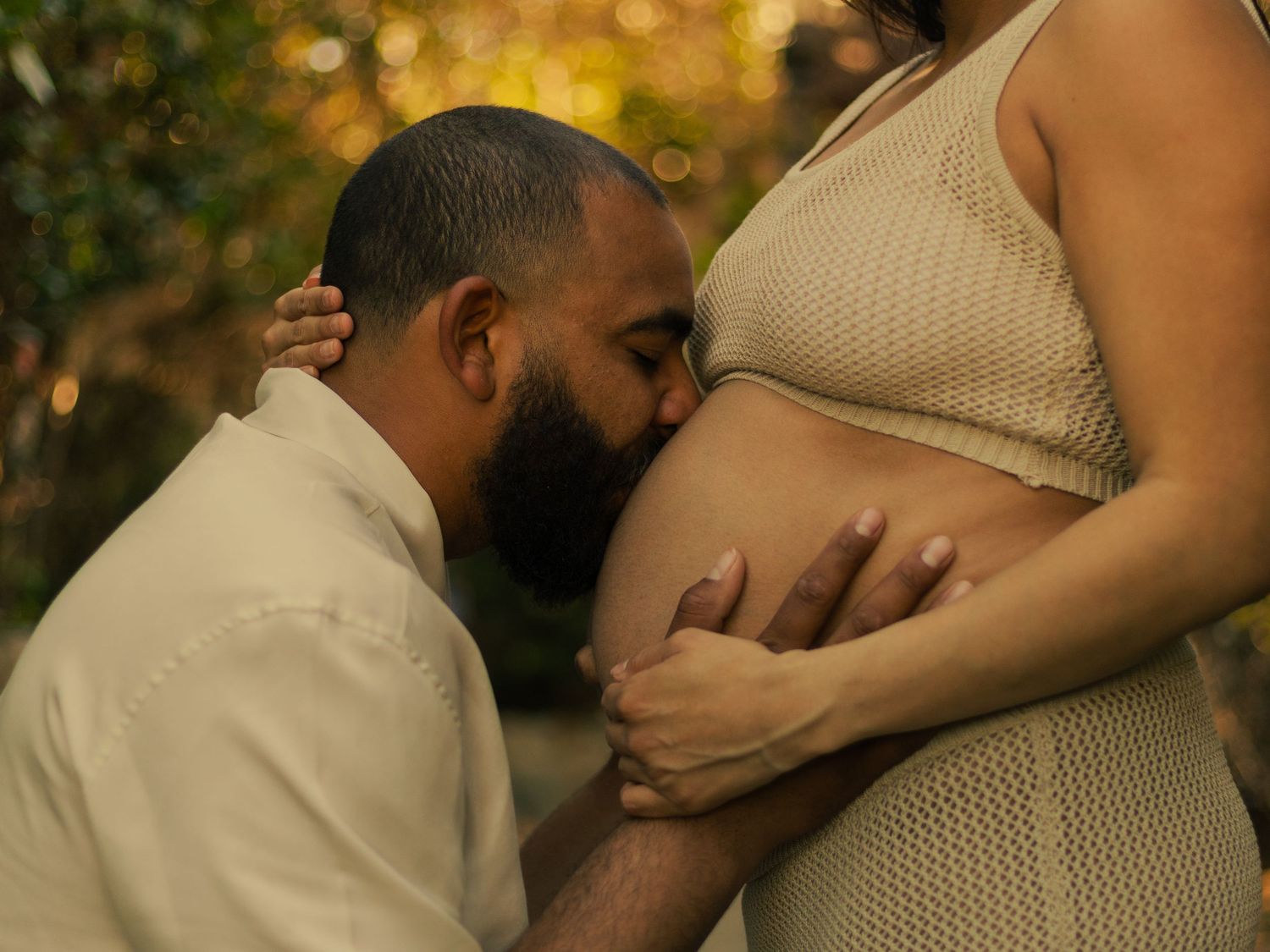Loving maternity documentary photography showing intimate moment with pregnant belly in warm golden sunset light.