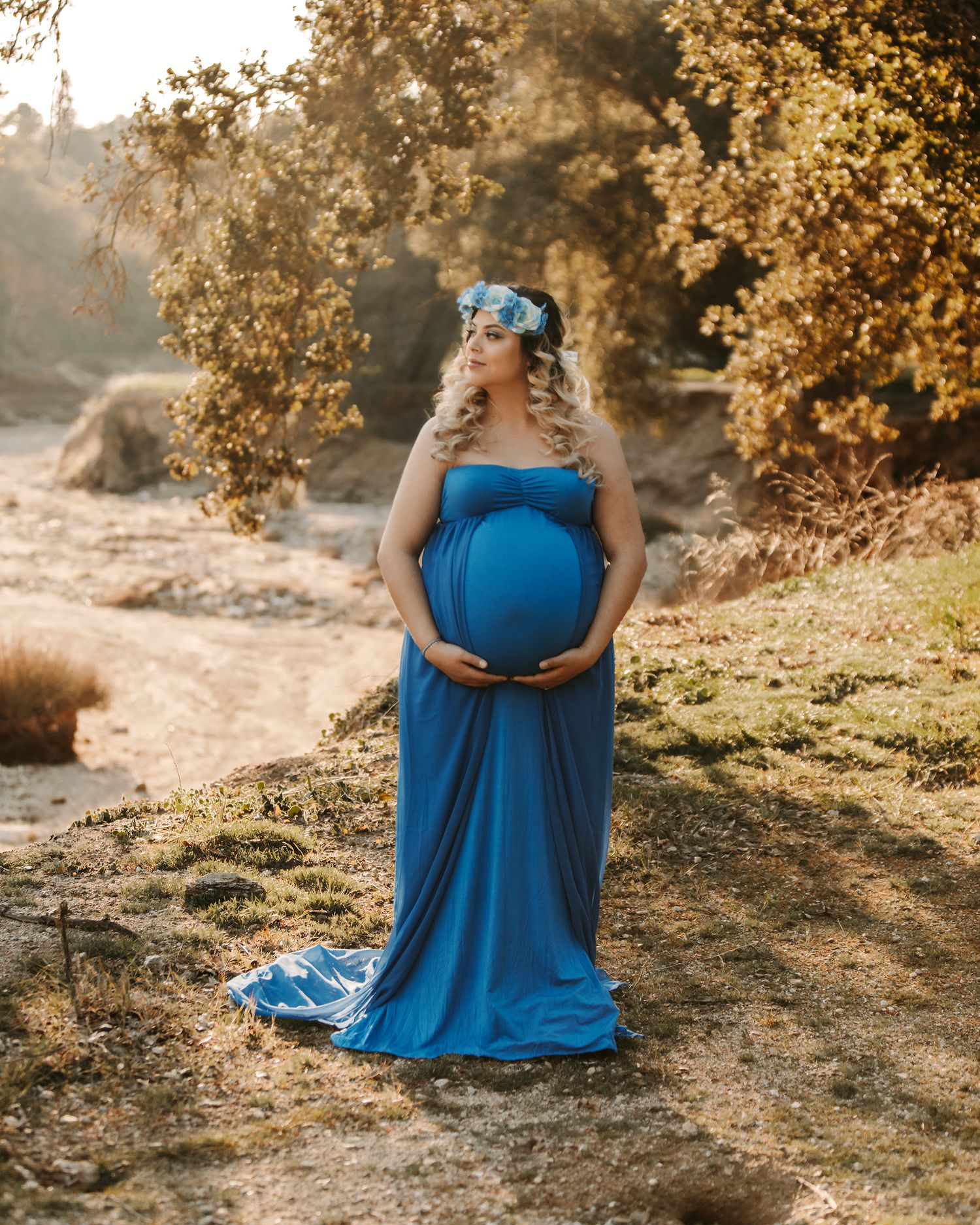 Maternity photography session in a flowing blue dress against autumn foliage.
