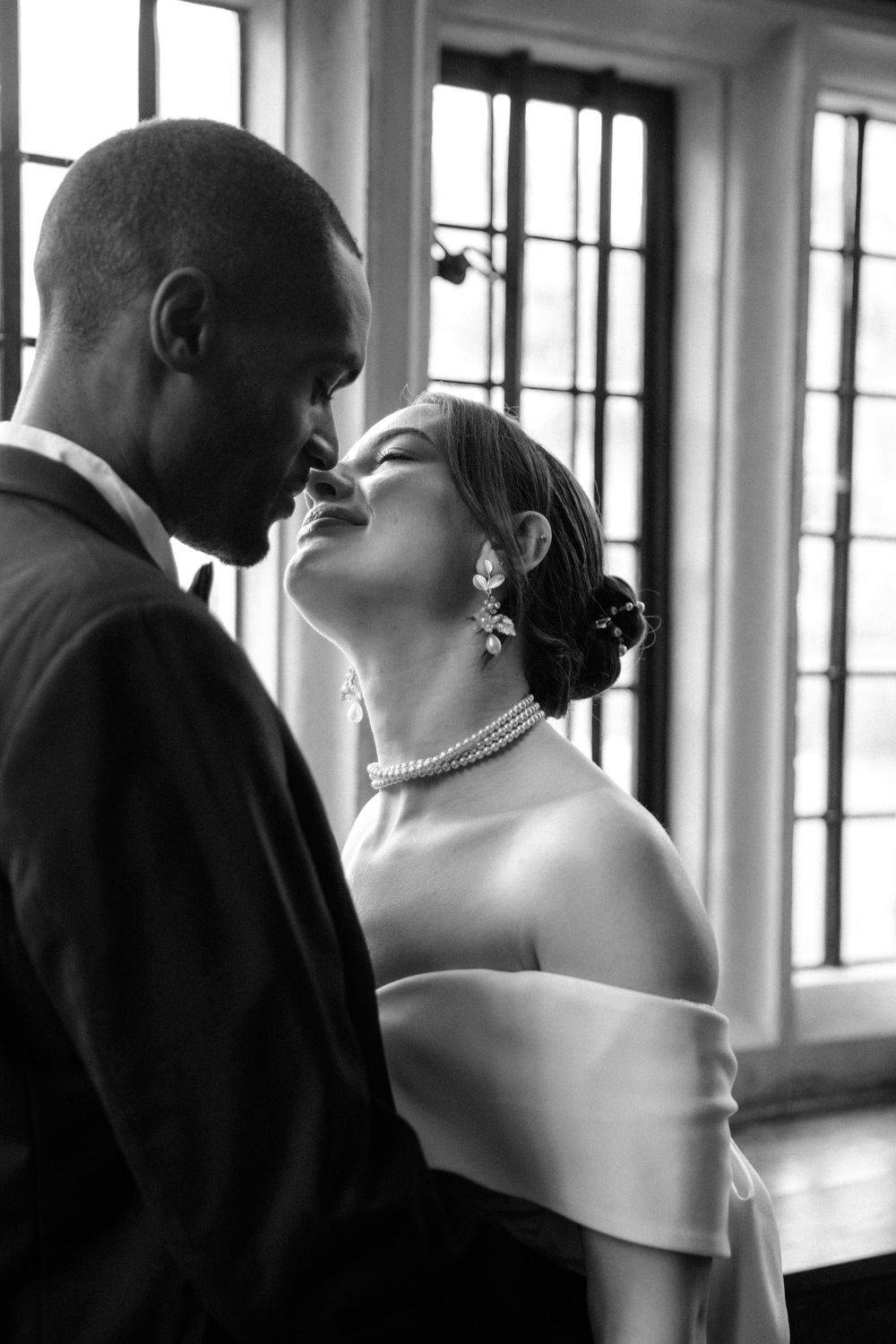 Romantic black and white portrait of newlyweds sharing an intimate moment by window.
