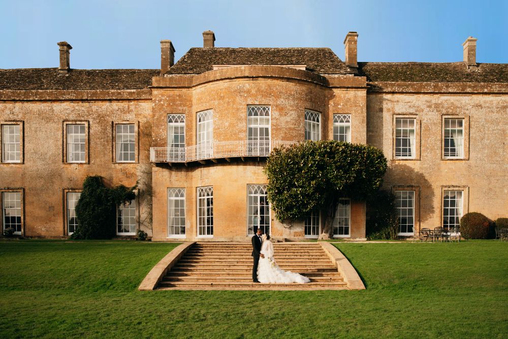 Elegant wedding couple poses on steps of historic Georgian mansion with manicured grounds.