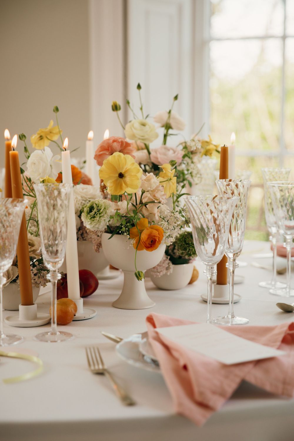 Wedding table setting with orange and yellow flowers, crystal glasses, and taper candles.