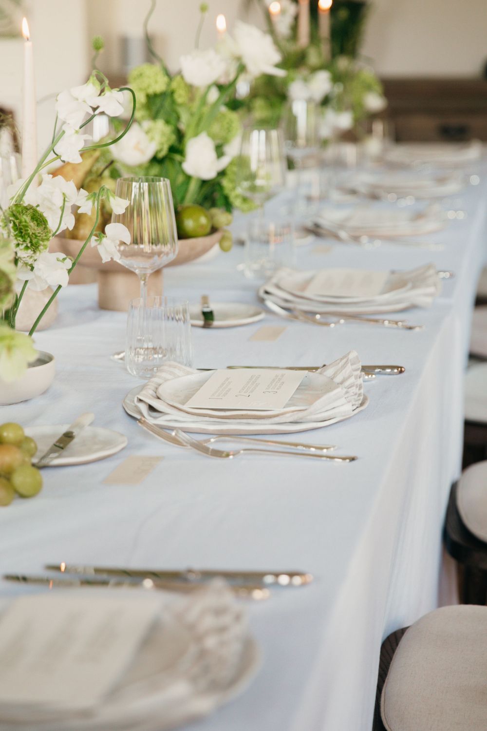Elegant table setting with white linens, fine china, and delicate floral arrangements.