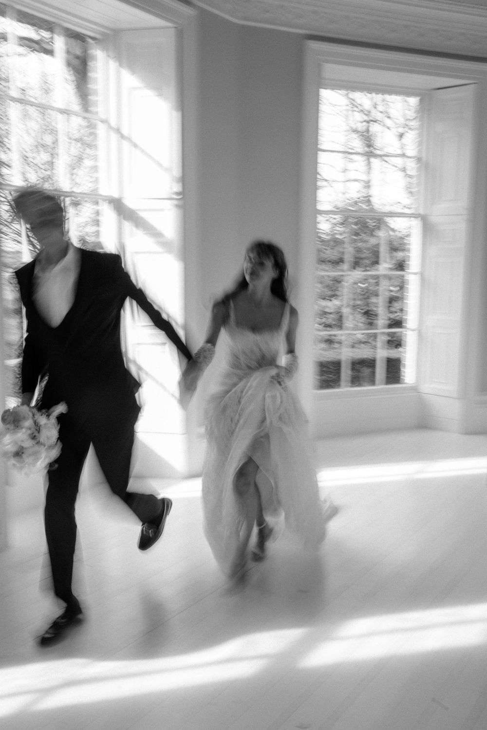 Motion-blurred photo of couple running through sunlit room in wedding attire.