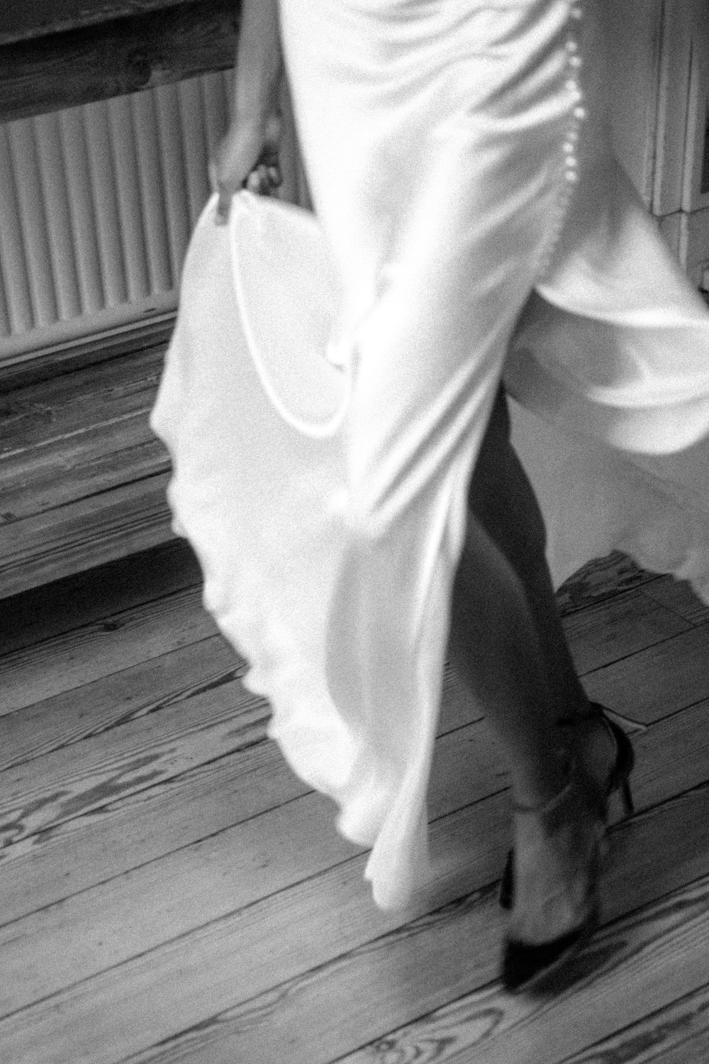 Black and white photo of flowing white wedding dress fabric and heels on wooden floorboards.