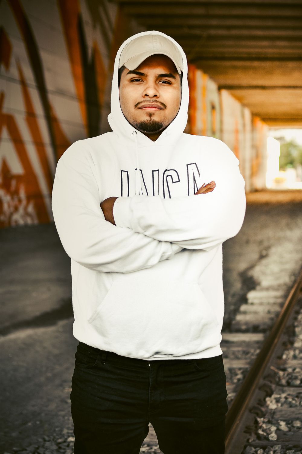 Man in white hoodie crossing his arms in the middle of train tracks.