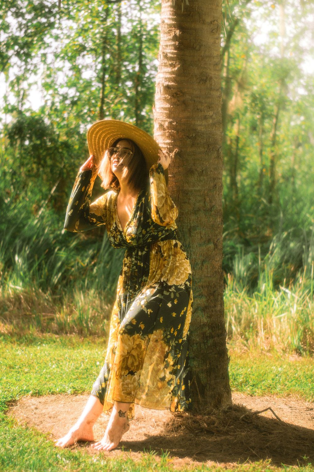 a woman posing in a sundress next to a palm tree
