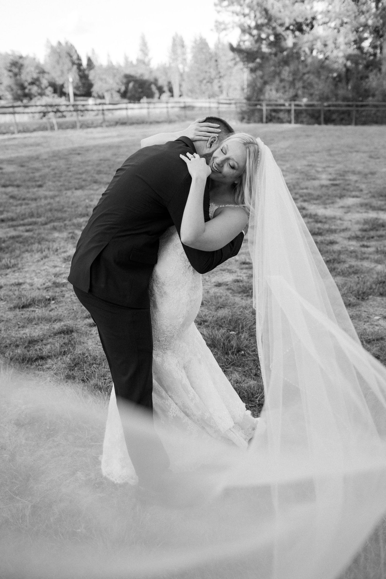 Black and white wedding photo of couple in romantic dip pose with flowing veil.
