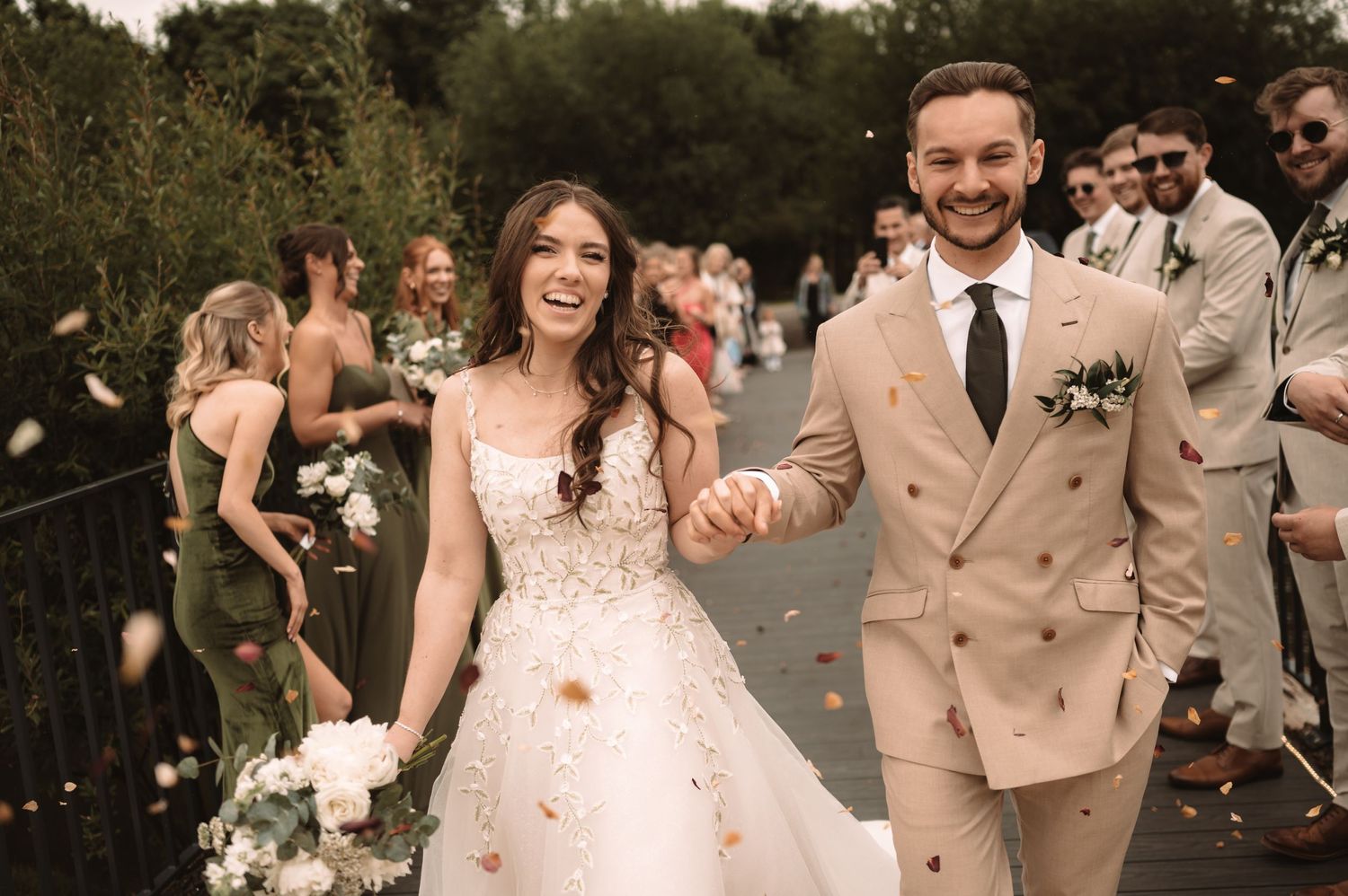 Wedding party celebrates on a paved path with confetti and joyful expressions.
