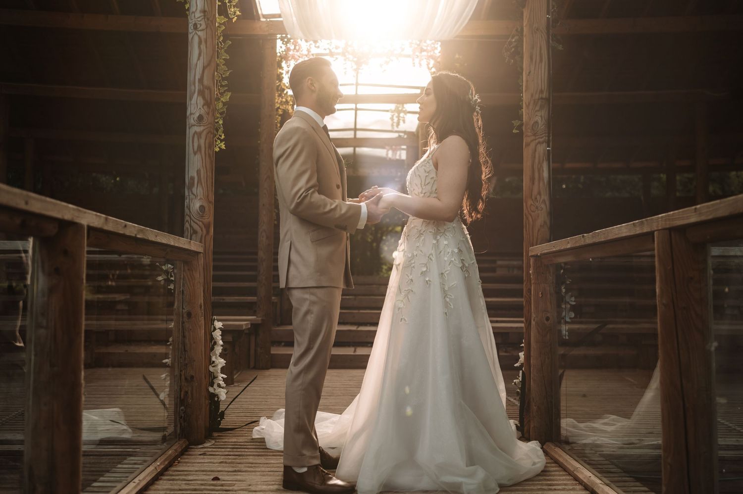 Wedding couple shares an intimate moment on a rustic wooden walkway at sunset.