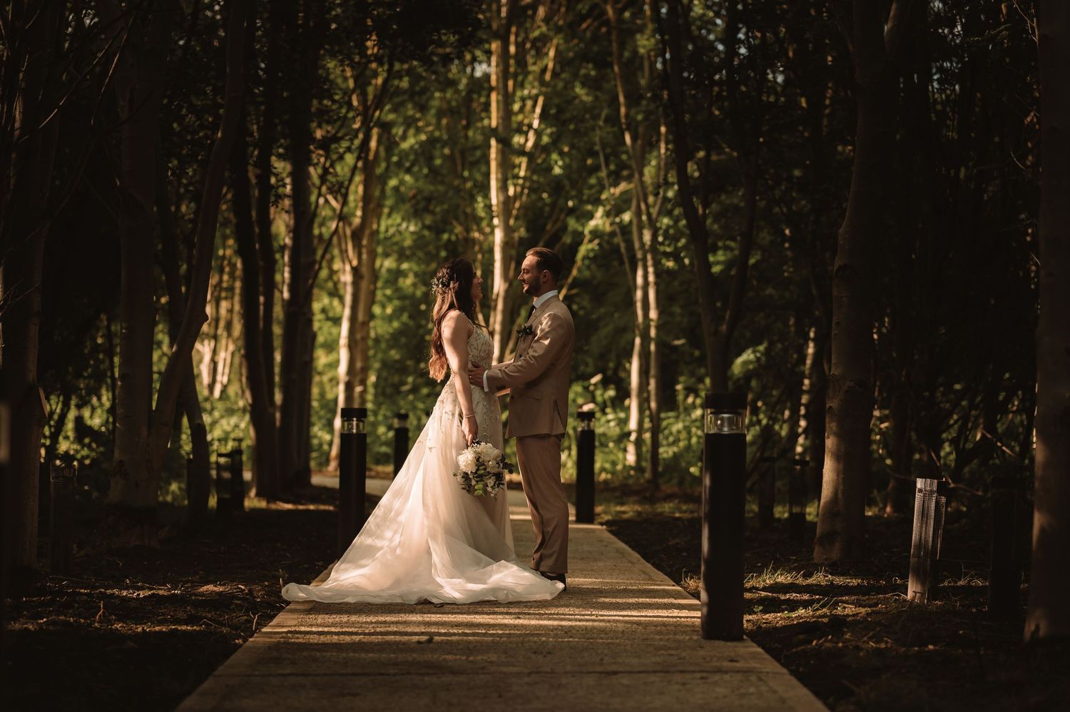 Wedding couple poses in a wooded setting with natural sunlight filtering through trees.