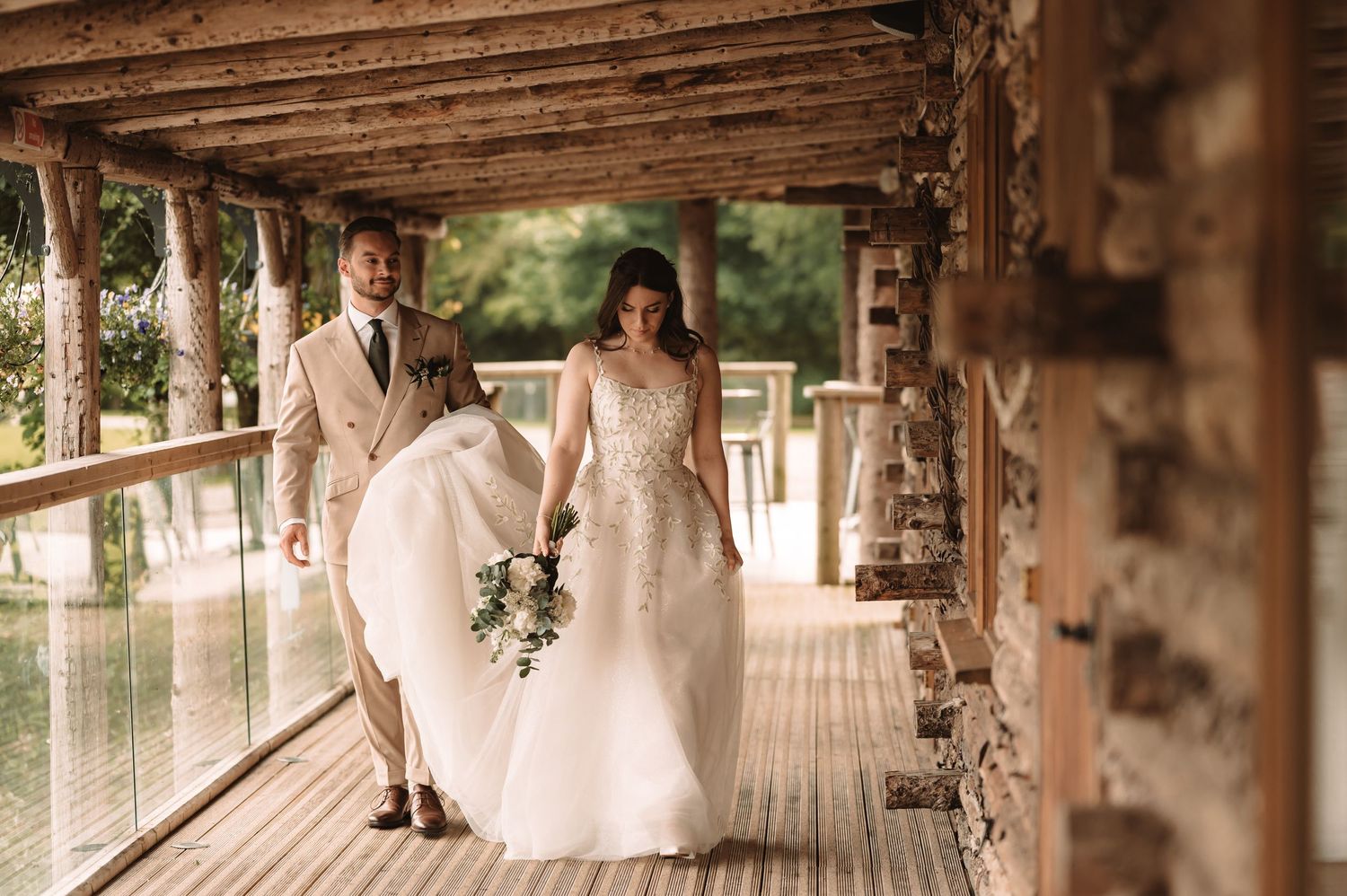 Wedding couple walks along a rustic wooden walkway decorated with white flowers.