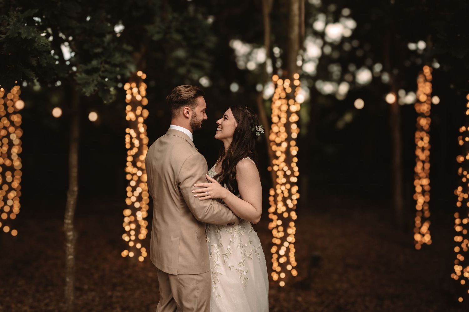 Romantic evening wedding portrait with string lights glowing in forest background.