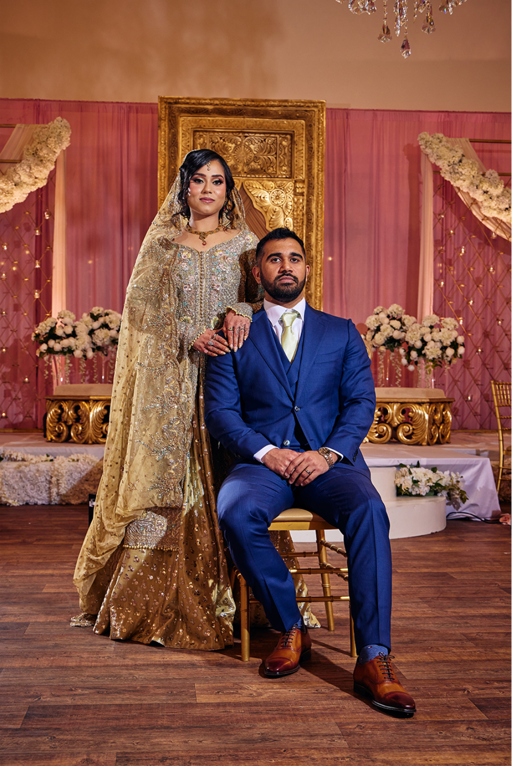 A formal wedding portrait featuring traditional South Asian attire with gold details and a royal blue suit.