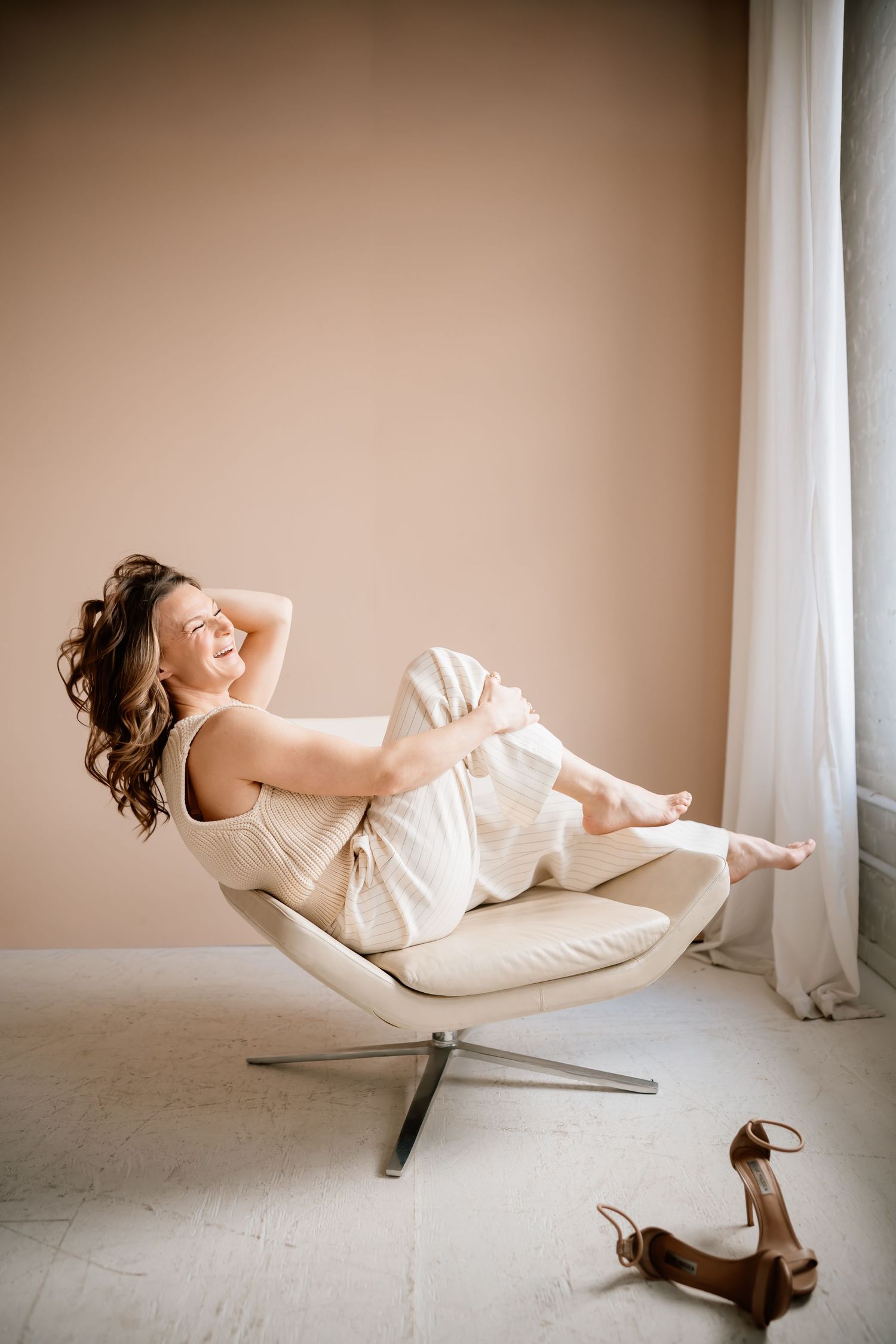 A person in white clothing performs a graceful reclining pose sequence on a minimalist chair against a beige wall.