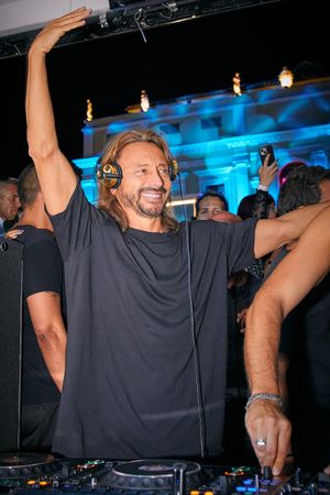 DJ wearing headphones performing enthusiastically behind decks with blue lighting in background.