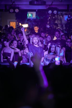 Energetic crowd at nightclub with purple lighting and raised hands during performance.