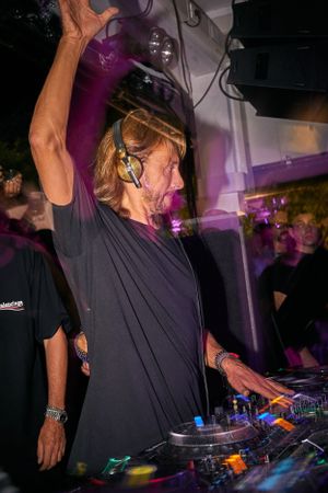 DJ performing at turntables in dark nightclub with purple lighting effects.