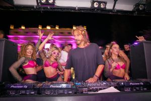 Nightclub scene with DJ performing at Pioneer decks while dancers celebrate.