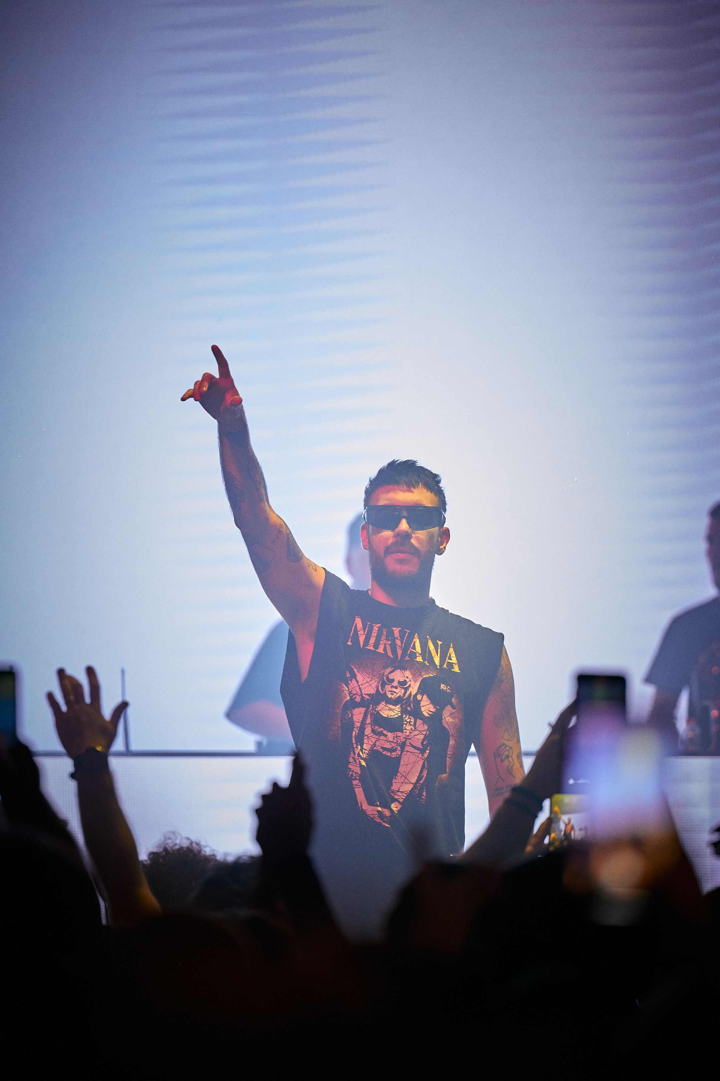 Performer wearing Nirvana shirt raises arm during concert as crowd cheers below.