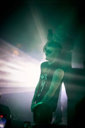Silhouette of performer in sunglasses and tank top under dramatic green stage lighting.