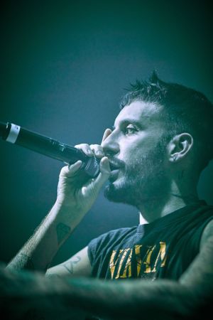 Close-up profile shot of performer singing into microphone with teal lighting effect.