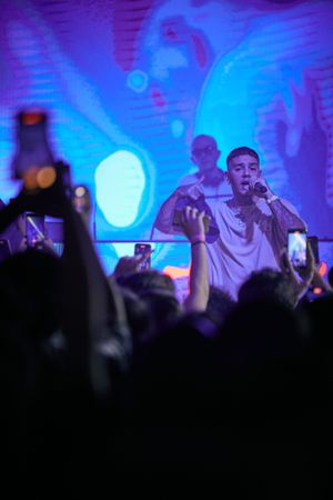Concert performer singing on stage with blue lighting effects and crowd holding phones up.