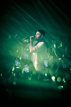 Concert performer on stage illuminated by bright green spotlights with crowd holding phones below.