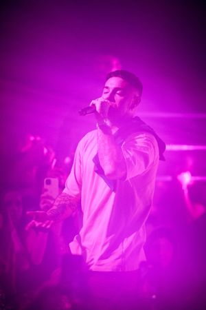 Singer performing on stage bathed in vibrant purple lighting during live concert.