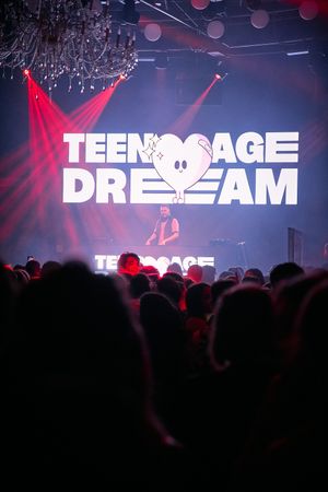 Teenage Dream logo displayed on stage with red lighting effects at a concert venue.