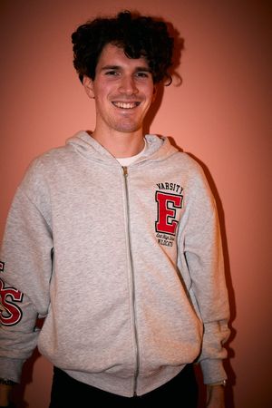 Person wearing grey university hoodie poses against orange background.