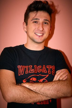 Person wearing a Wildcats t-shirt poses against an orange background.