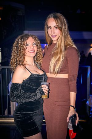 Two club-goers posing together at a nightlife venue with dark lighting.